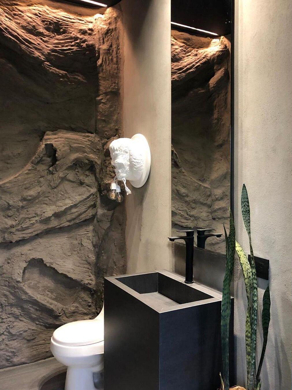 Wide rock-wall washroom with white gorilla light, mirror, black basin and toilet