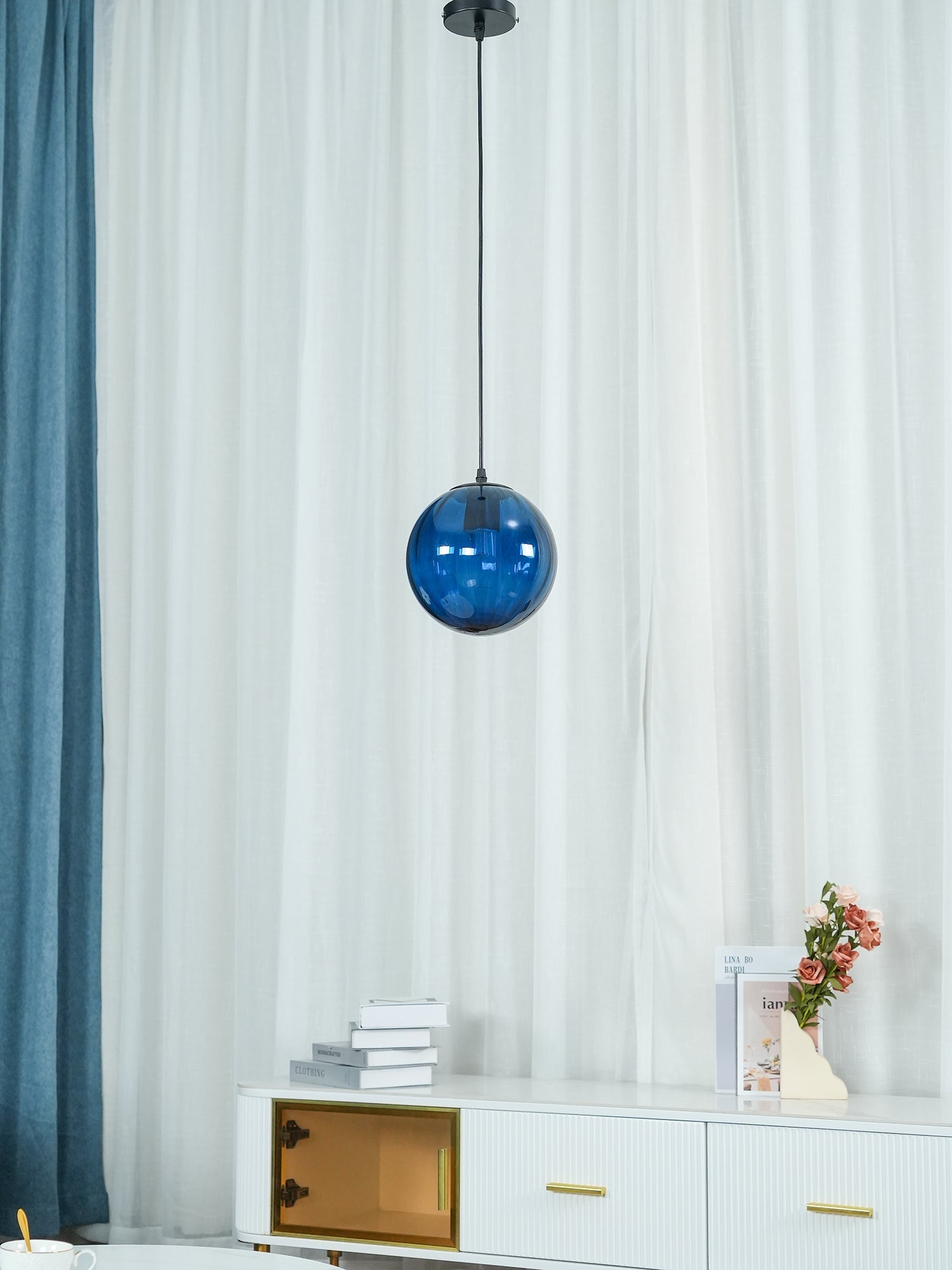 Small blue glass pendant suspended beside curtains