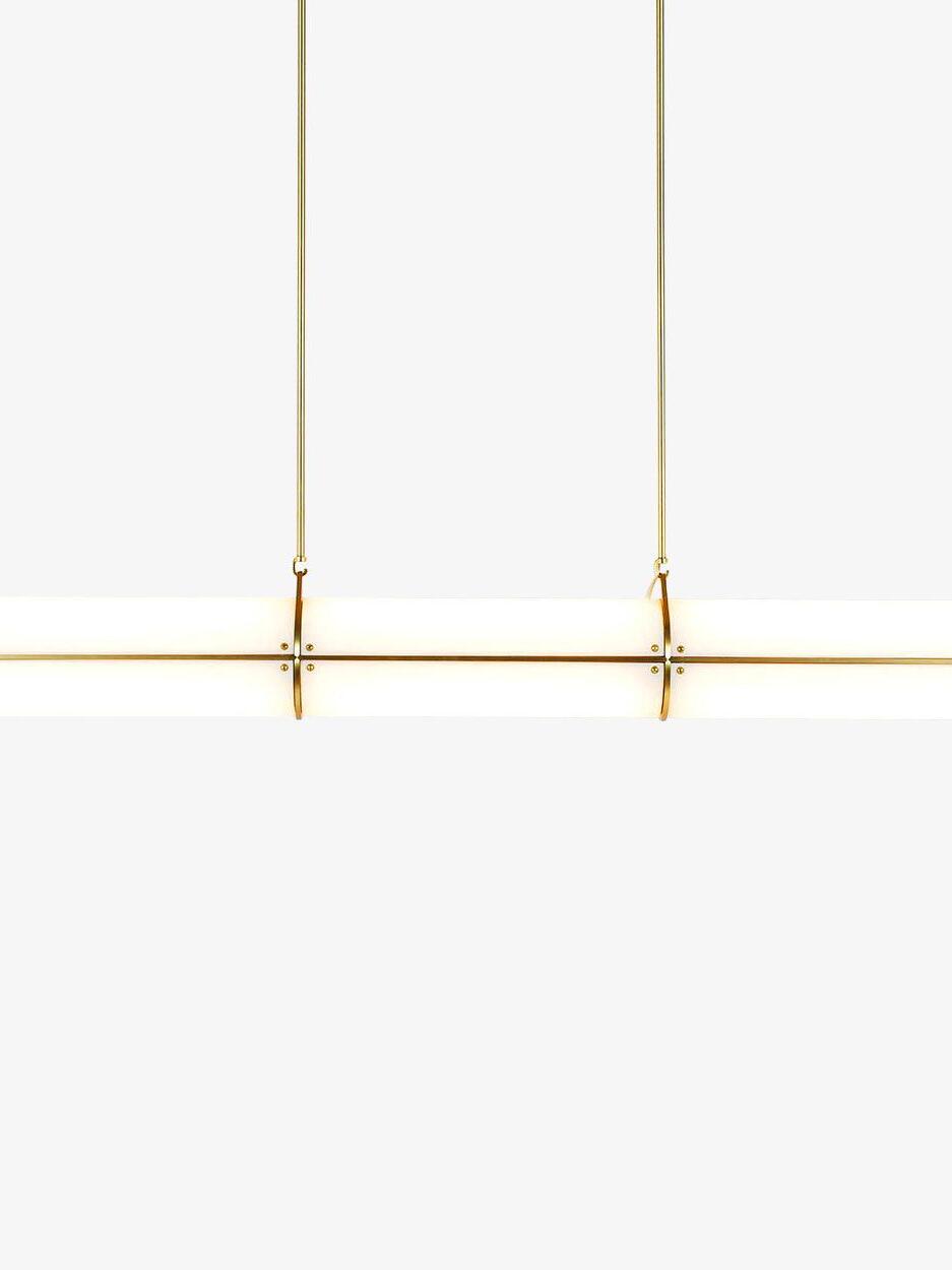 Front close-up of a lit cylindrical shade with a gold rail, two ring bands and two hanging supports on white