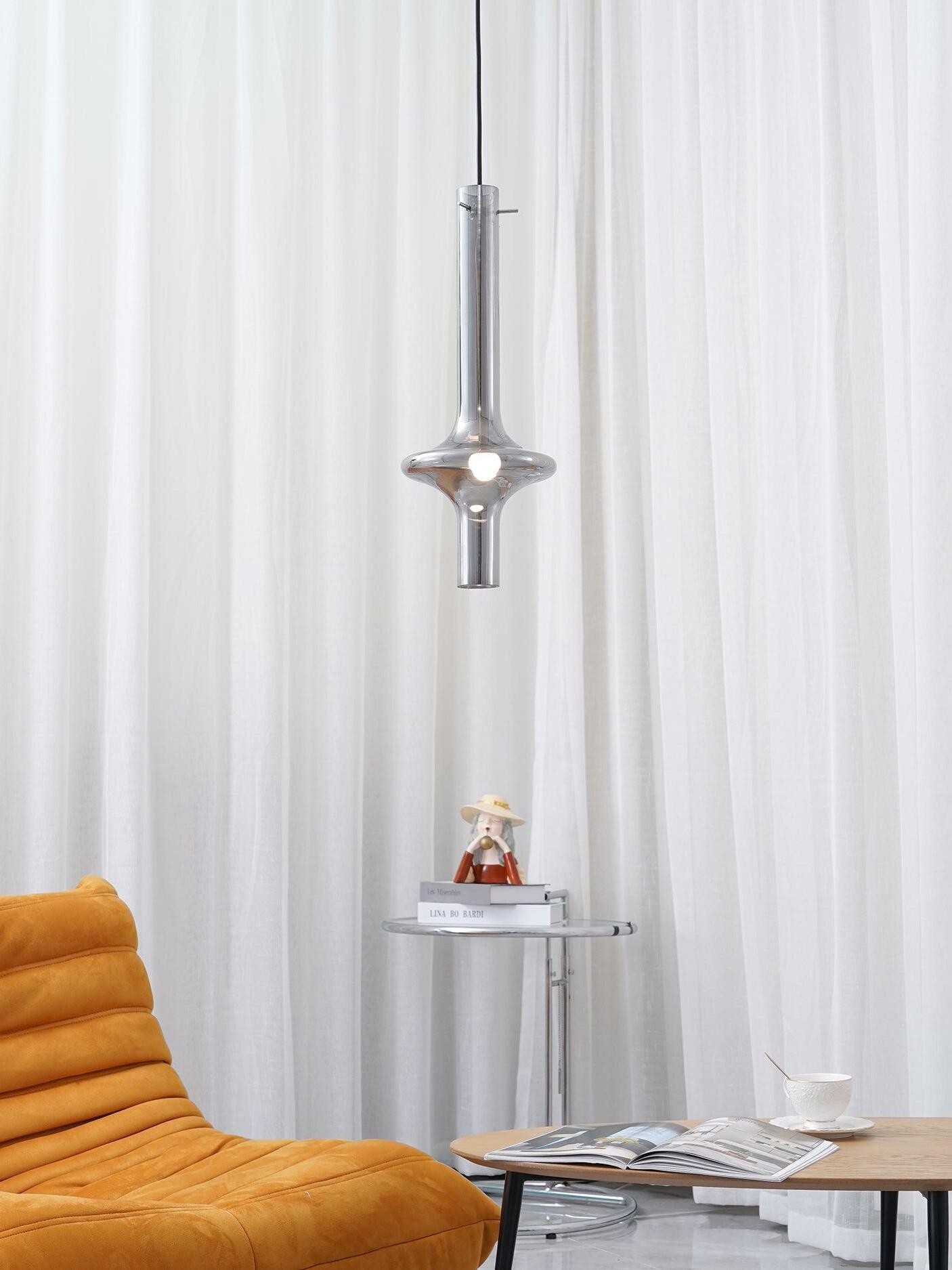 Lit smoky glass pendant above an orange chair and side table, with white curtains, books, figurine and coffee table