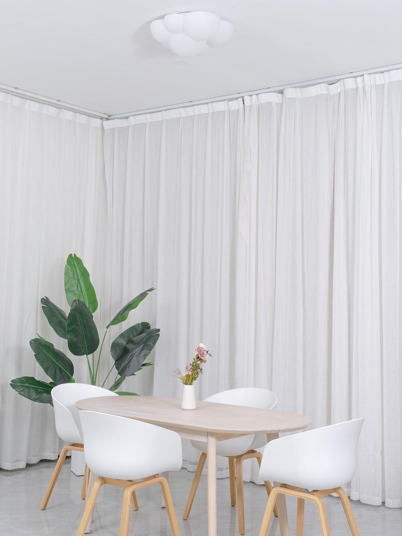 Unlit white Nuage ceiling light above a dining table beside full-height curtains