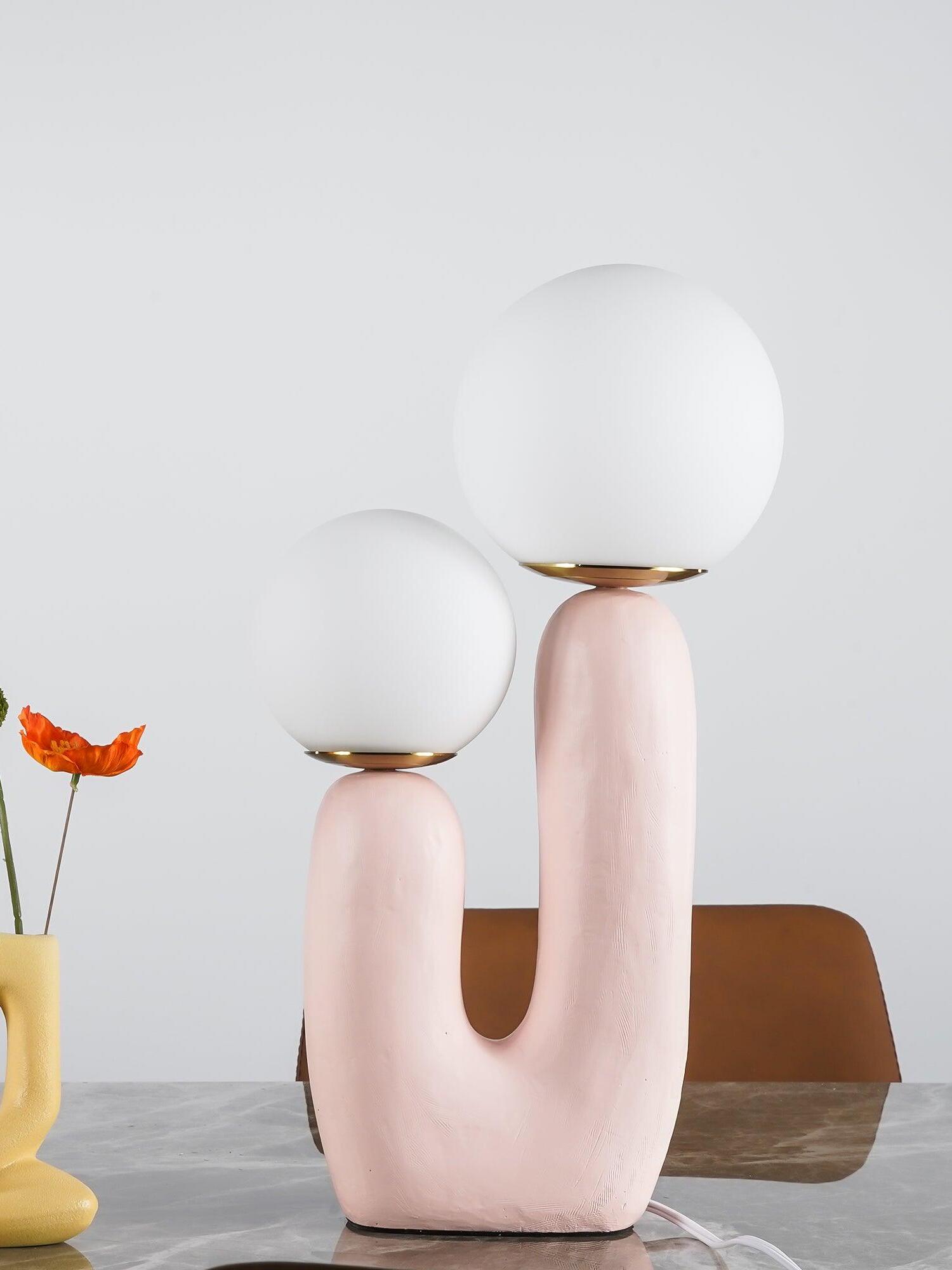 Pale pink Oo Rough lamp with two white opal globes on marble beside a yellow vase and orange flower
