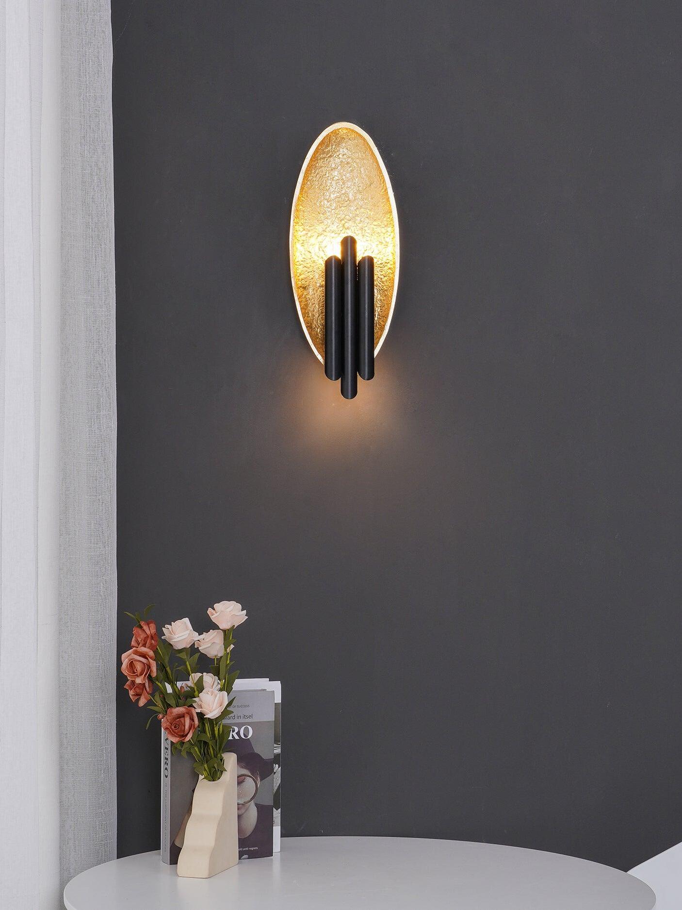 Lit dark-and-gold oval wall light above white table and flowers