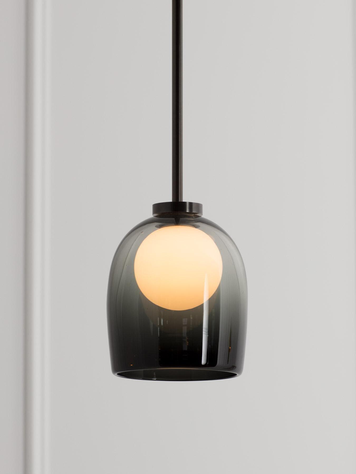 Closer view of the illuminated sphere and gradient-black bell shade of a Crux pendant
