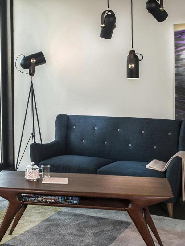 Black pendant heads above a blue sofa and wooden coffee table, with a related tripod floor lamp beside the window