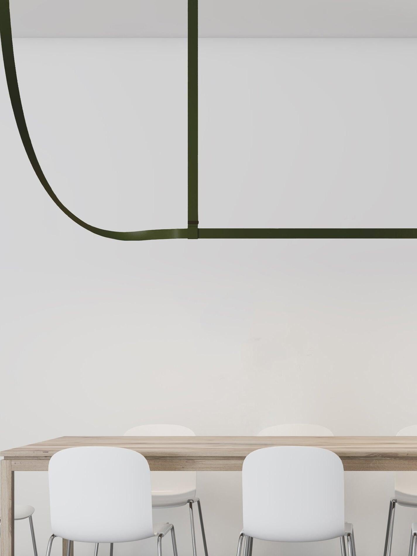 Close view of a green horizontal bar, upright strap and curved belt end above a wood table and pale chairs