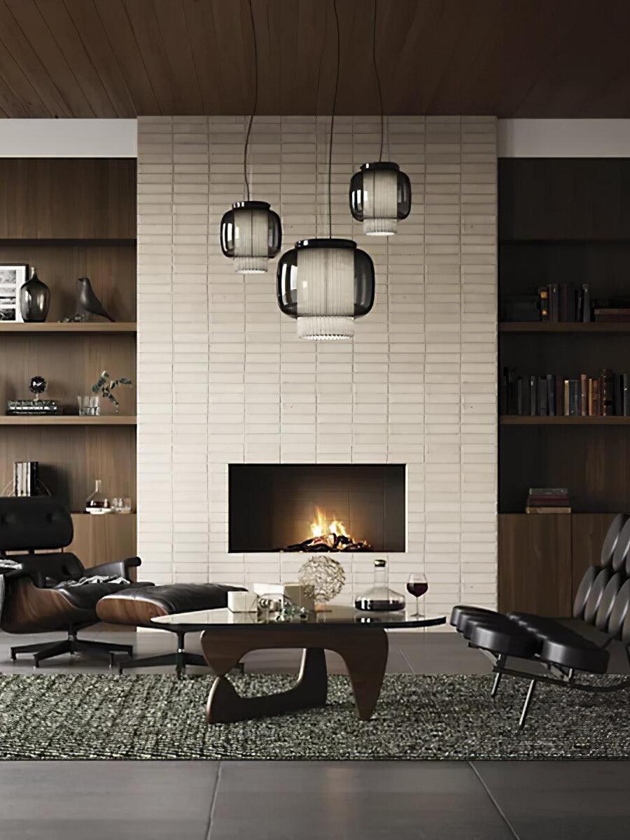 Wide lounge view of three Manila T pendants above a coffee table near a white brick fireplace and leather chair