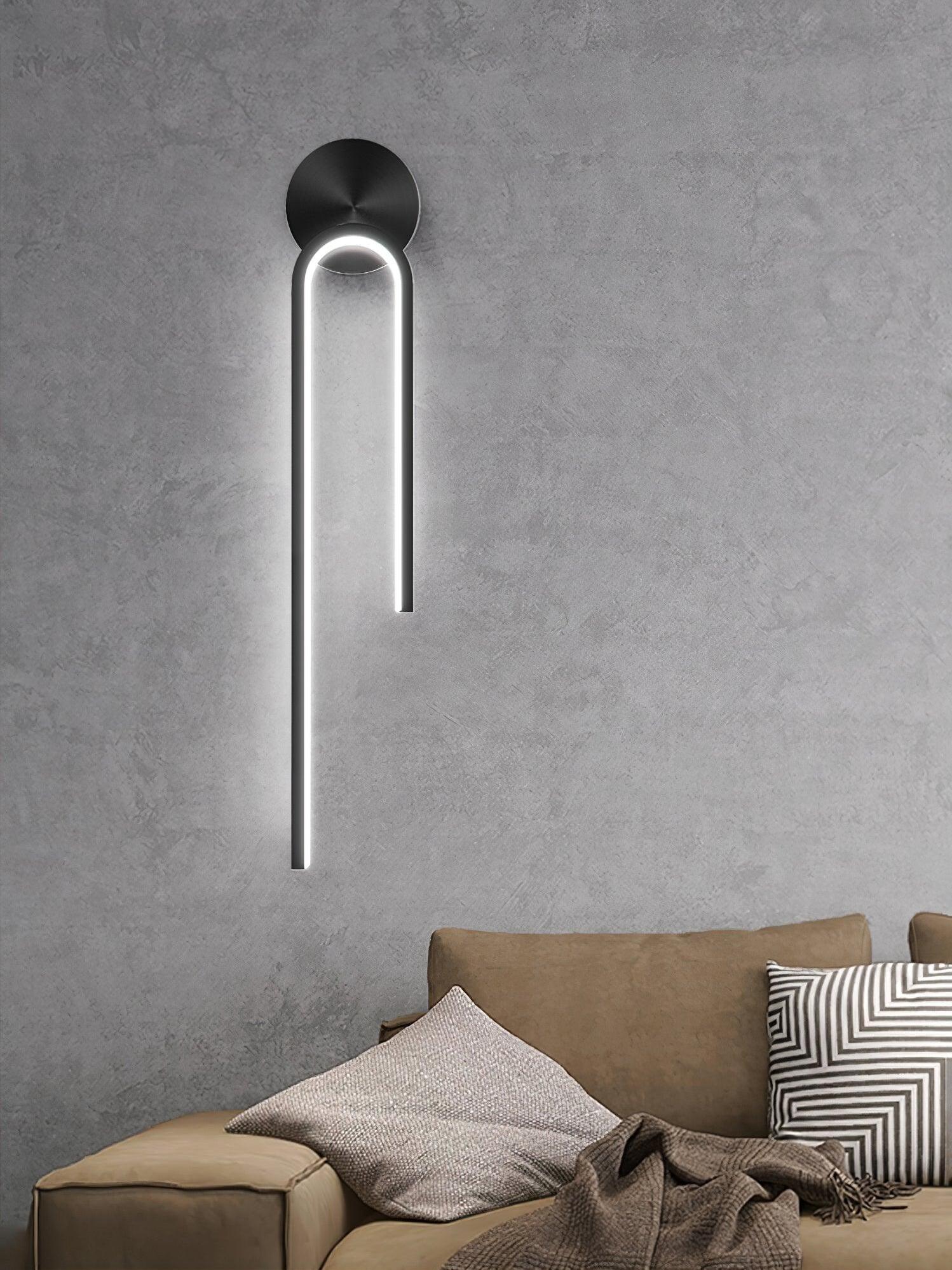 Black arch wall light with a long left arm above a brown sofa and patterned cushions on a textured wall