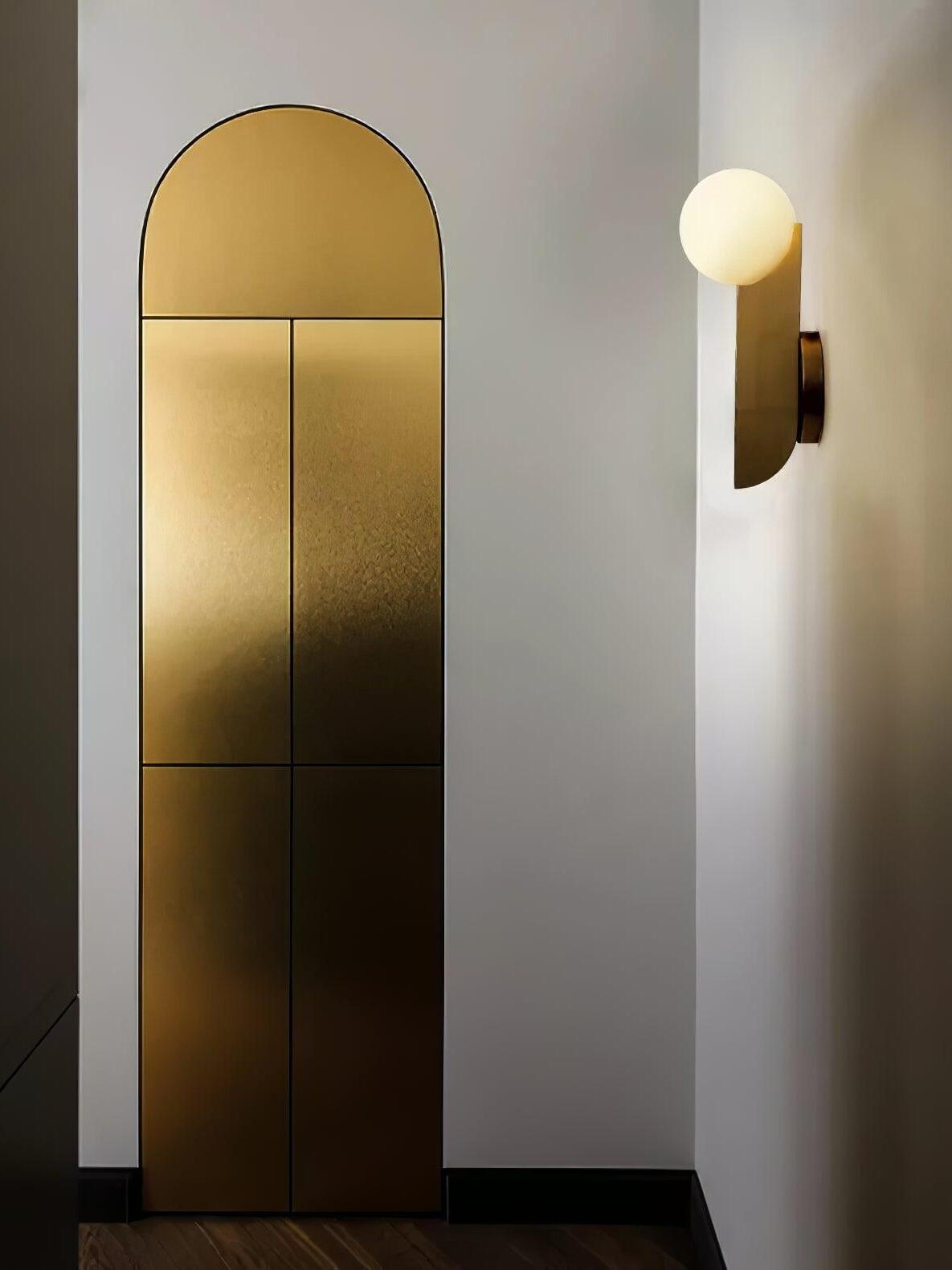 Lit globe and gold-colour blade wall lamp beside an arched gold panel in a hallway