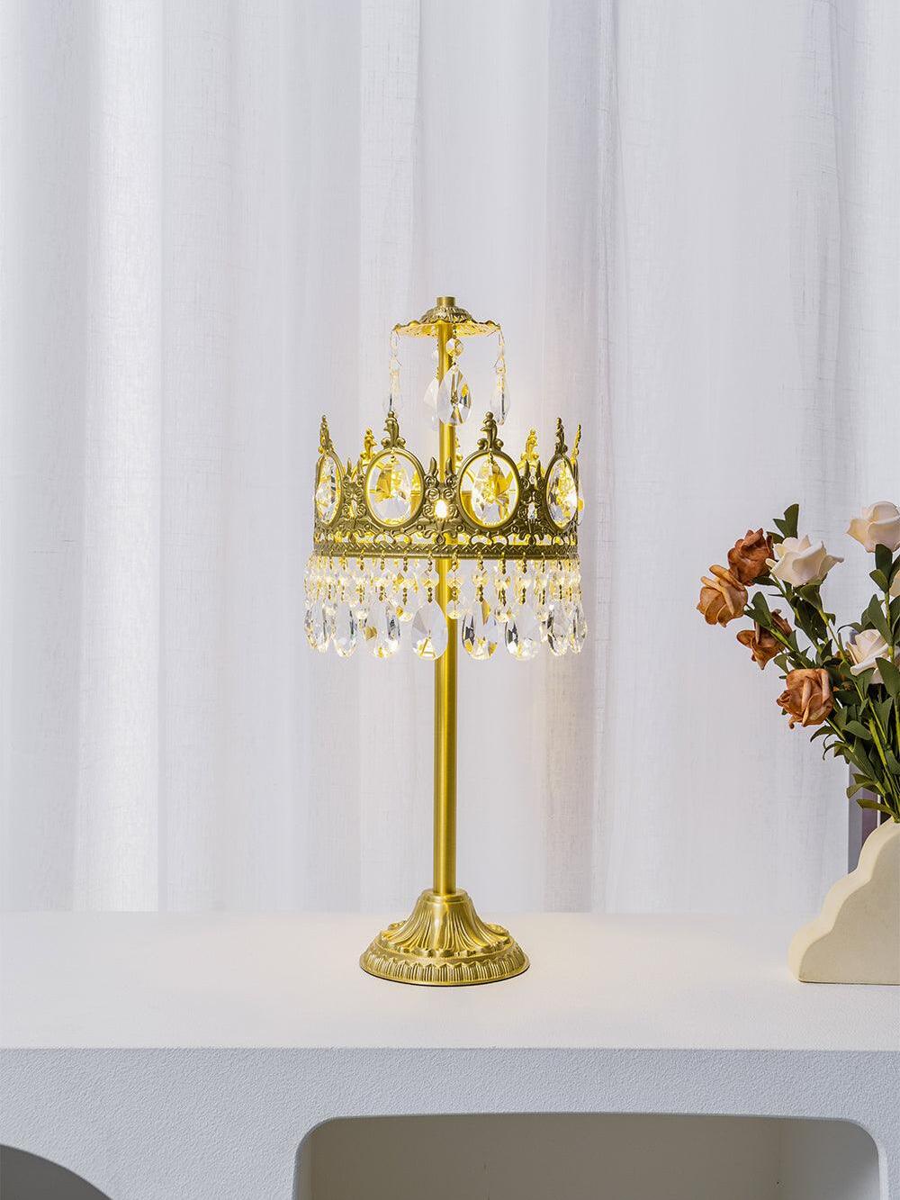 Lit crystal table lamp on a white console, with flowers beside the hanging crystal fringe.