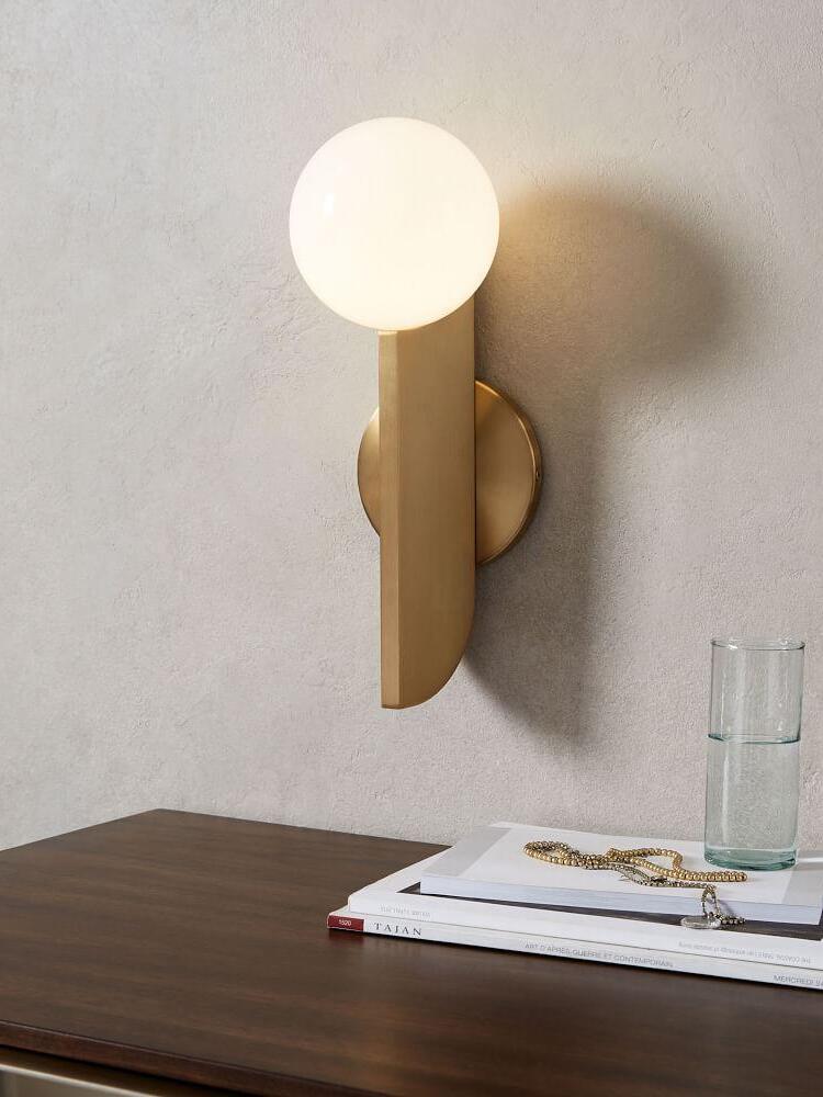 Lit globe wall lamp above books, jewellery and a water glass on a dark wooden surface