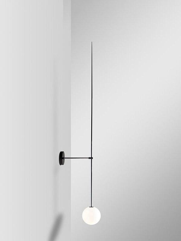 Angled black rod wall light with a short wall arm and white globe against a pale wall