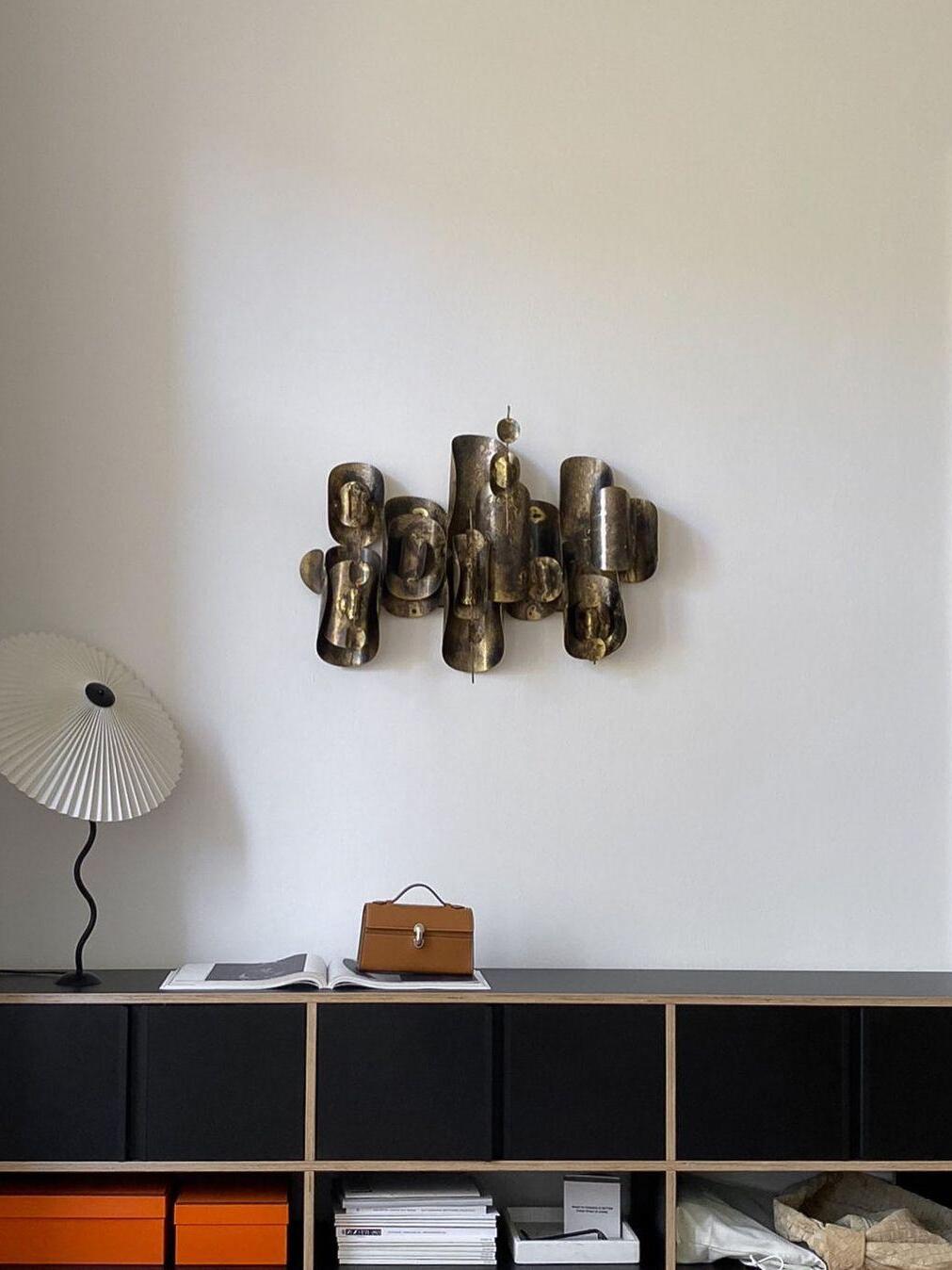 White-shade Squiggle lamp on a black modular sideboard beneath a metallic wall sculpture