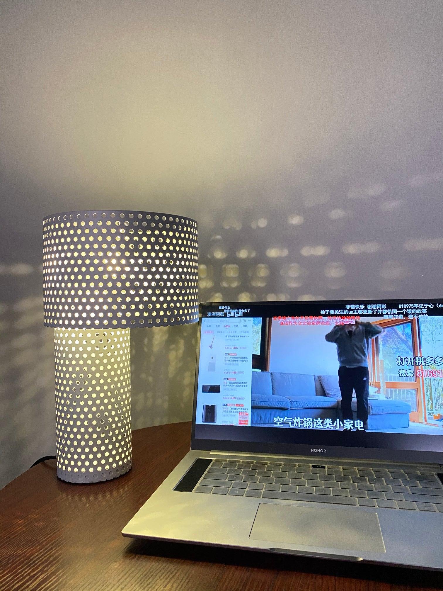 Lit table lamp and spotted wall shadows by laptop