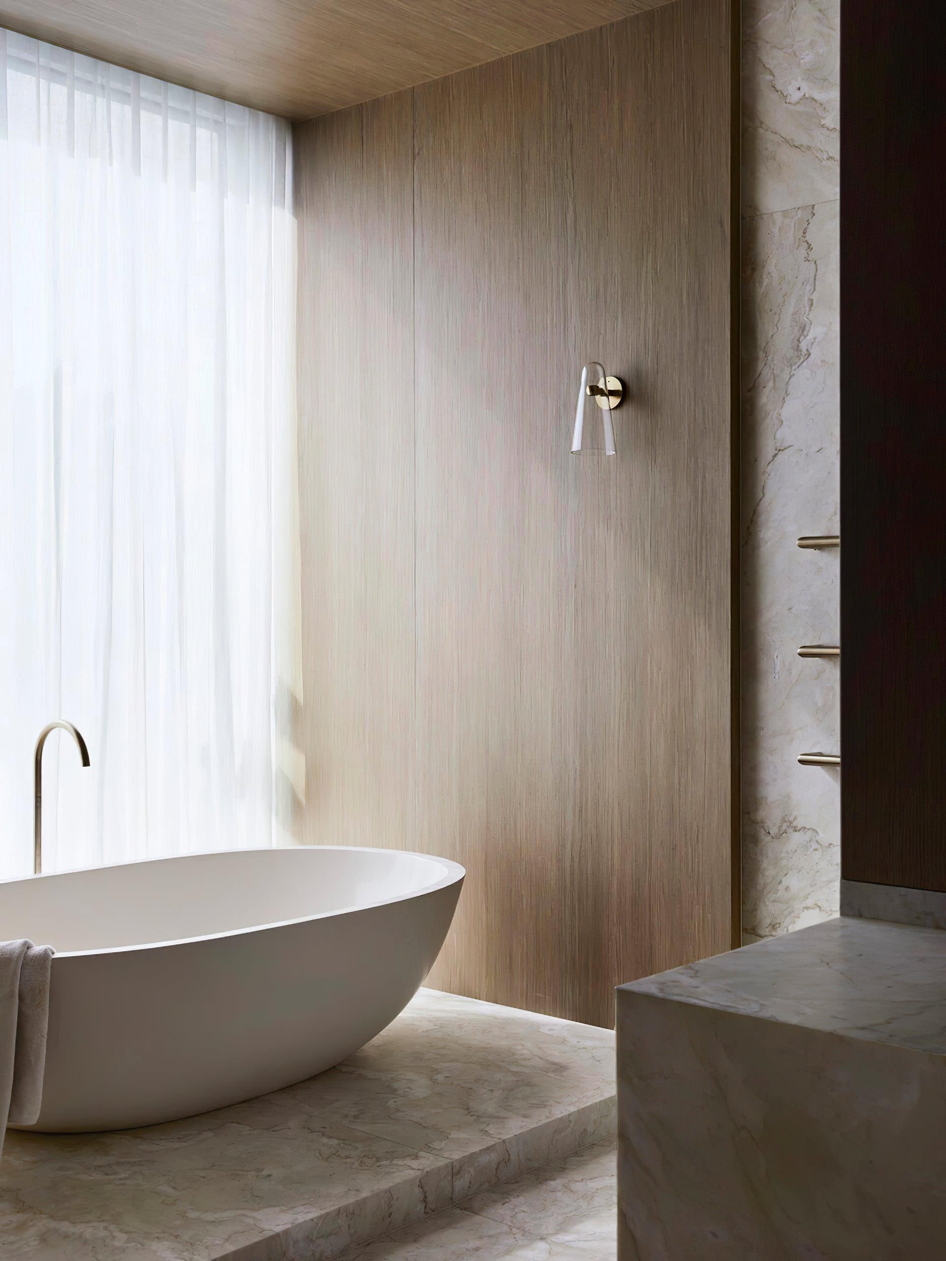 Small wall fixture above a bath beside sheer curtains