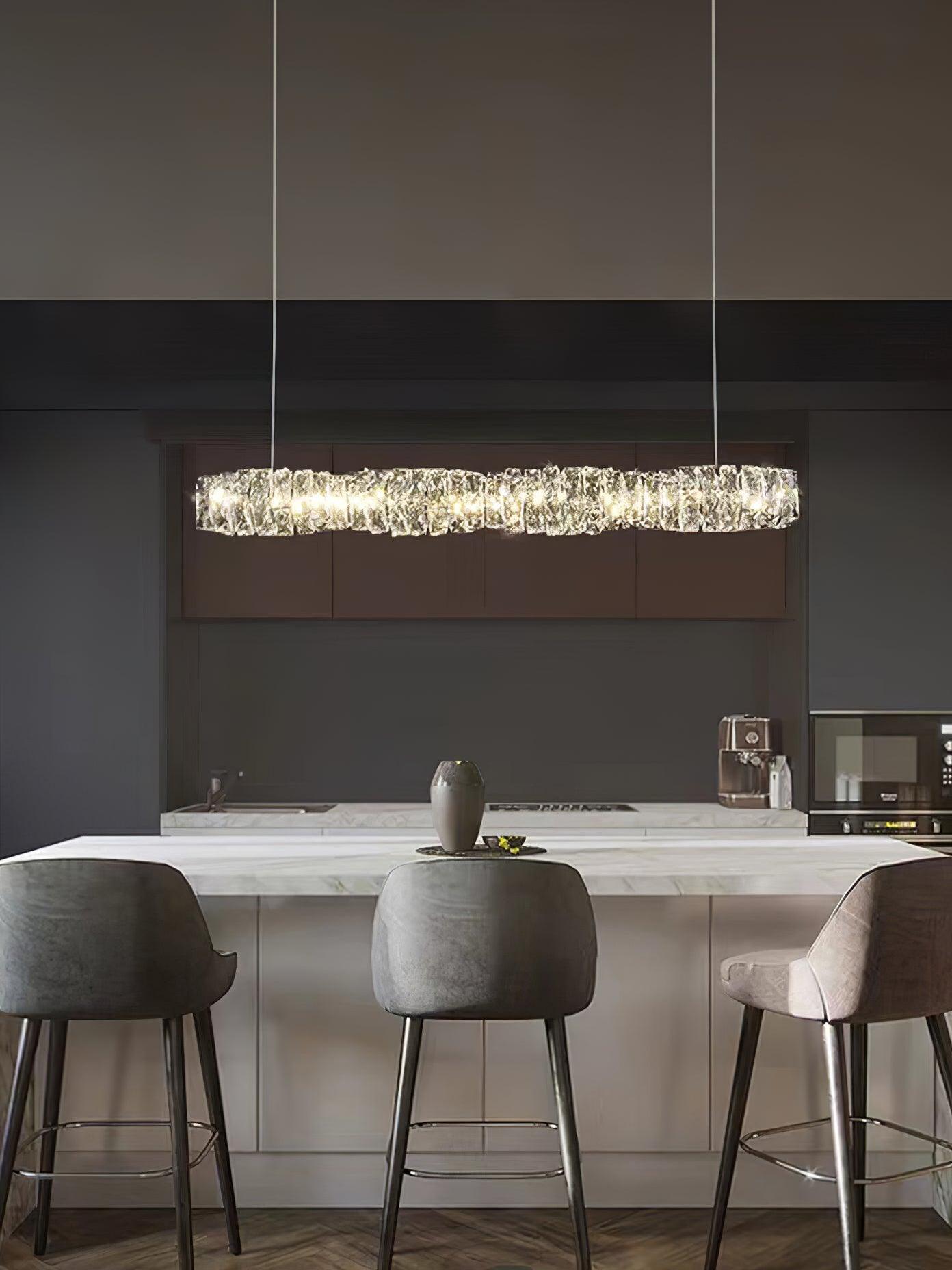 Front view of the long crystal pendant above a kitchen island with pale upholstered stools