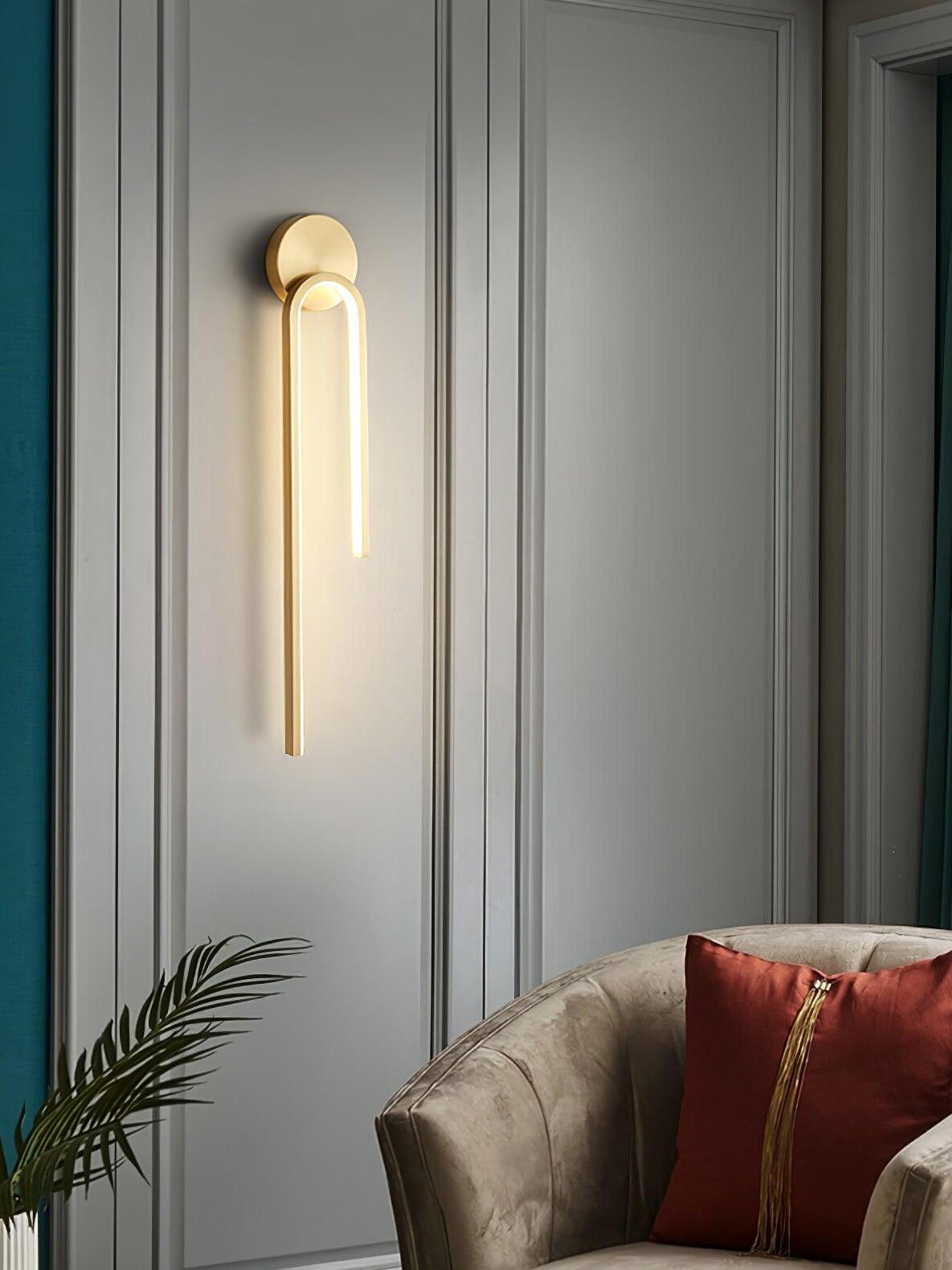 Gold-tone arch wall light above a cream chair, red tassel cushion and plant beside gray wall panels