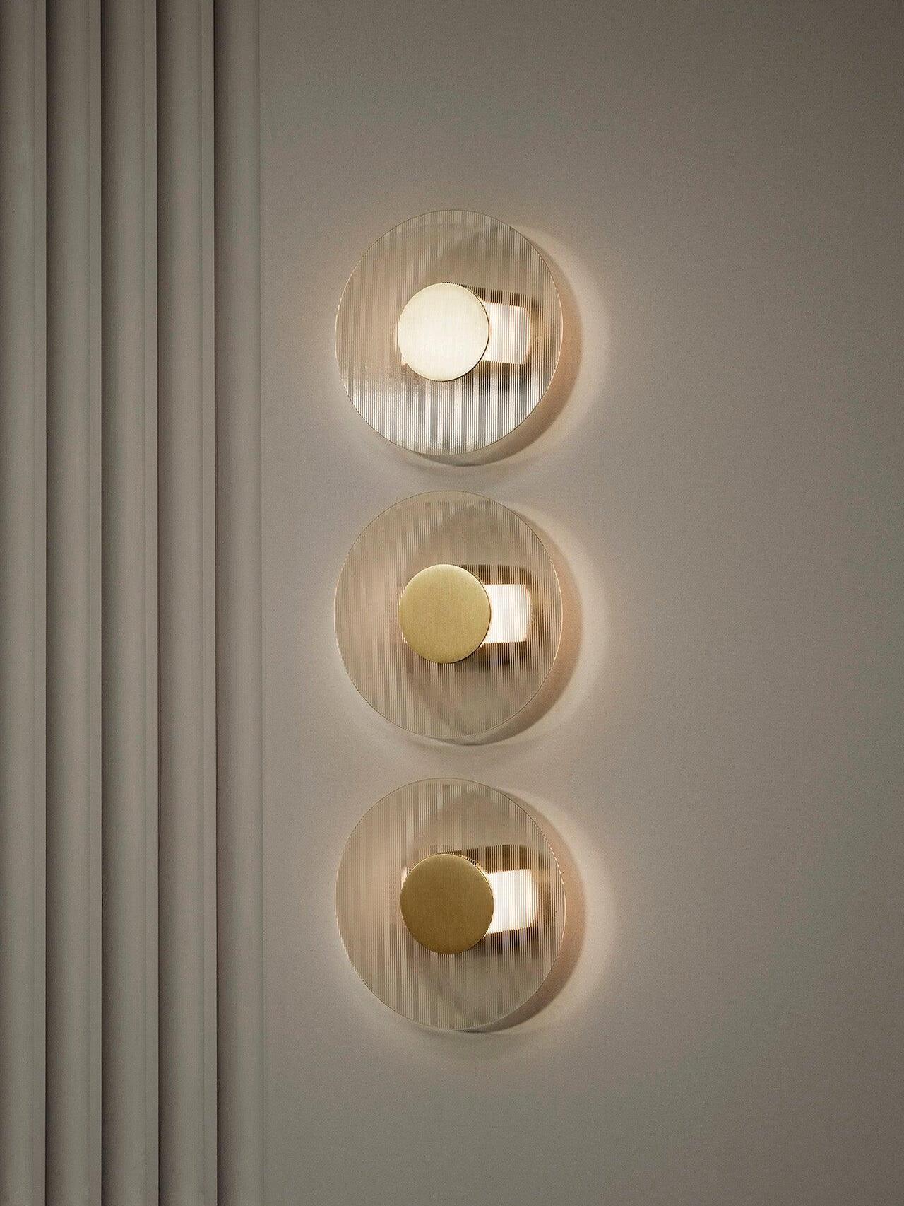 Close frontal view of three round Button wall lights stacked vertically beside a fluted pale wall