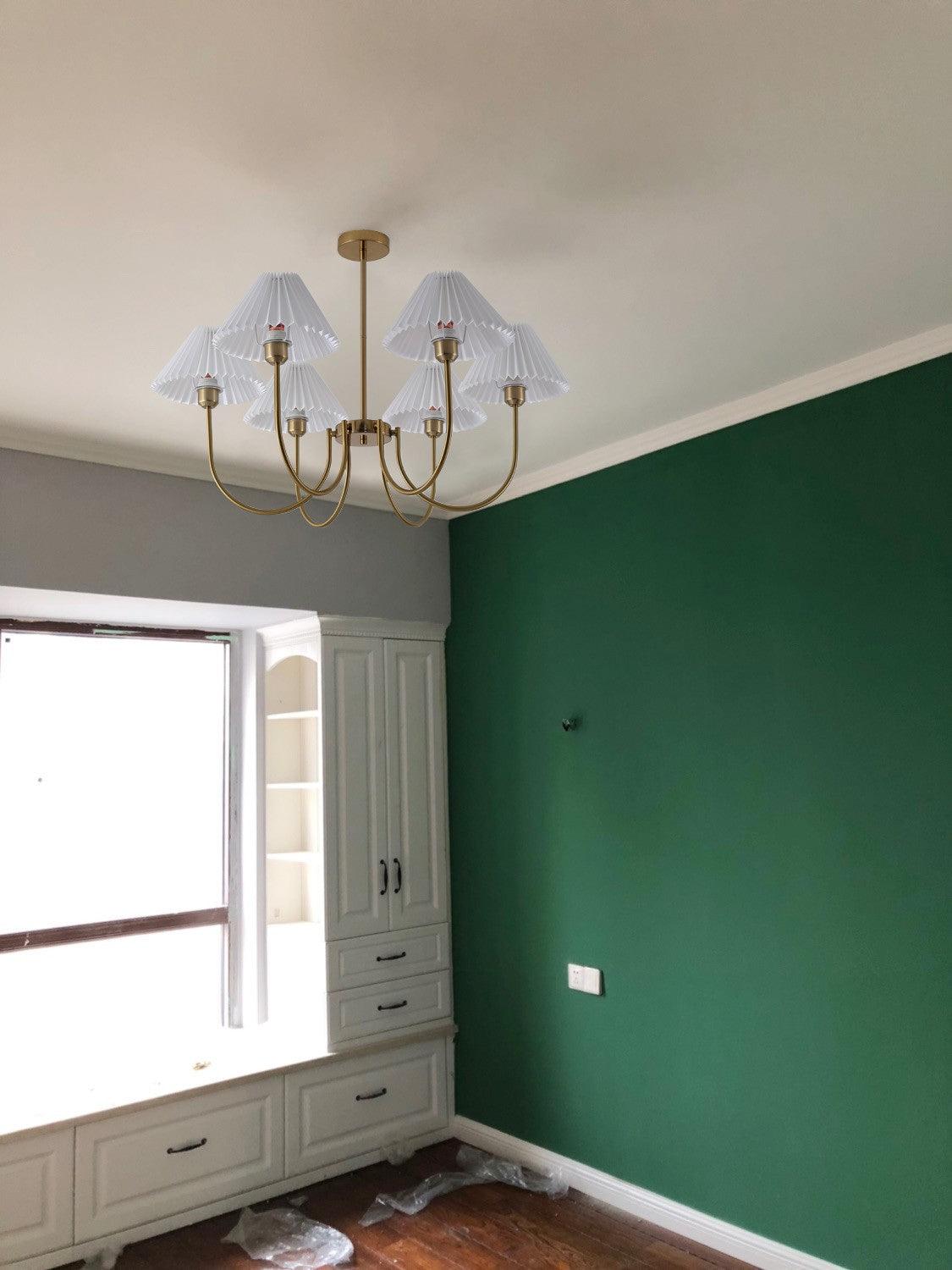 Unlit pleated-shade chandelier in a room with a green wall and low window cabinet