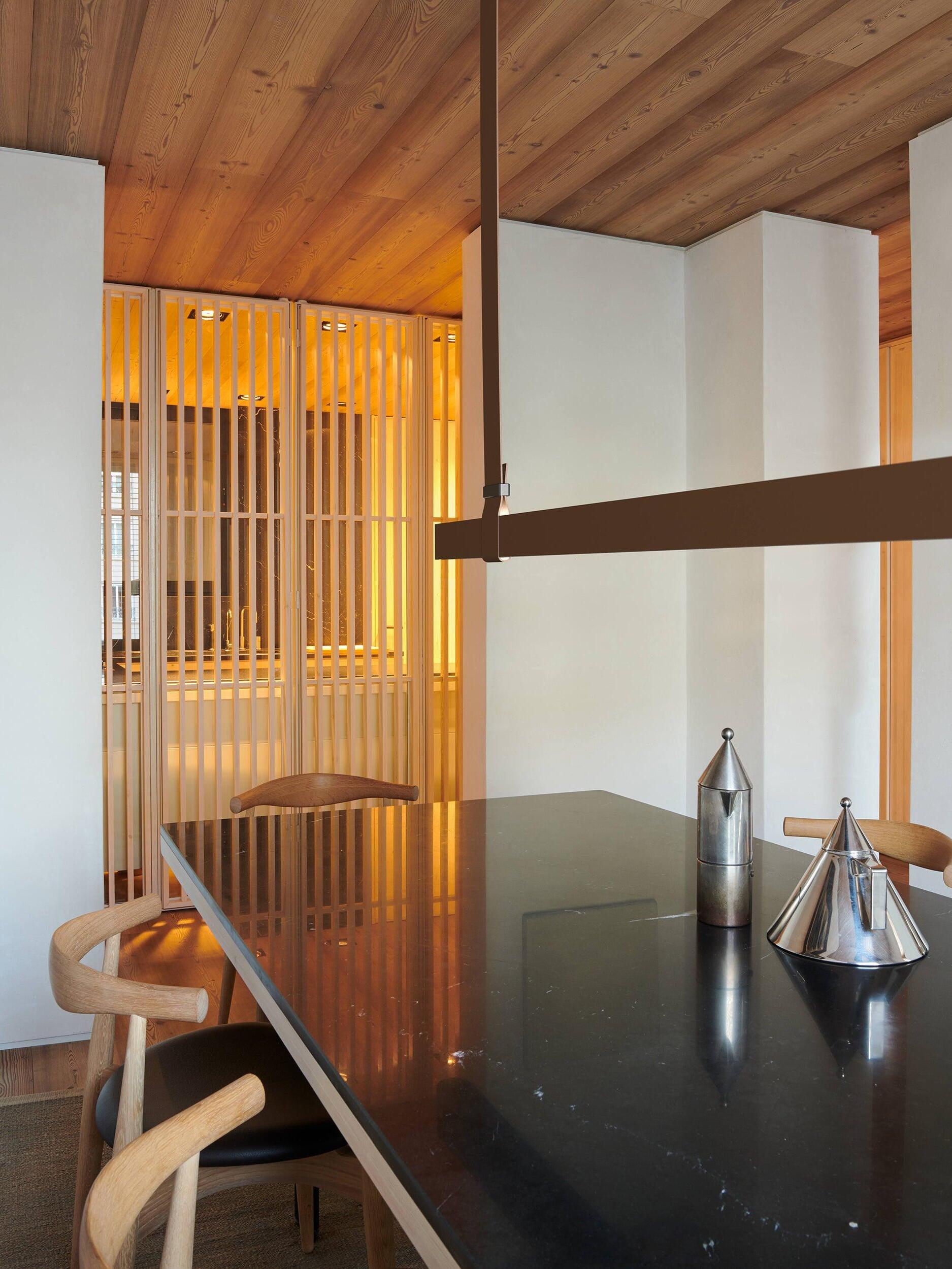 Brown pendant bar and vertical strap connector above a glossy black dining table with wood chairs and metal vessels