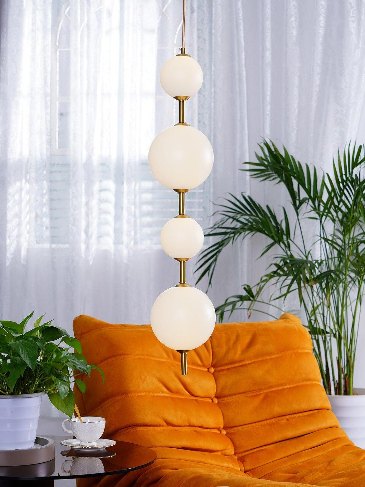 Four lit white globes in a vertical line before sheer curtains and plants above an orange chair