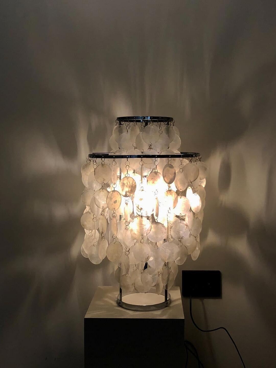 Lit shell lamp on narrow cabinet casting wall patterns