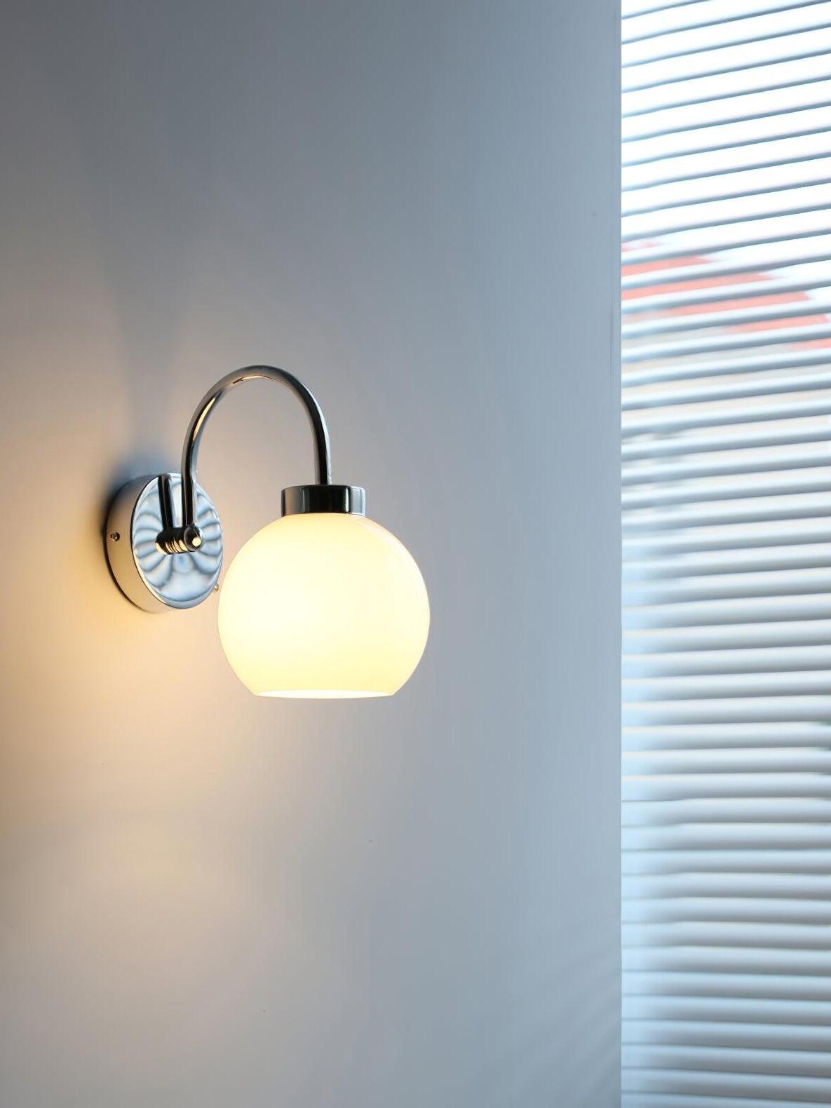 Lit pale white glass globe on curved wall arm beside window blinds