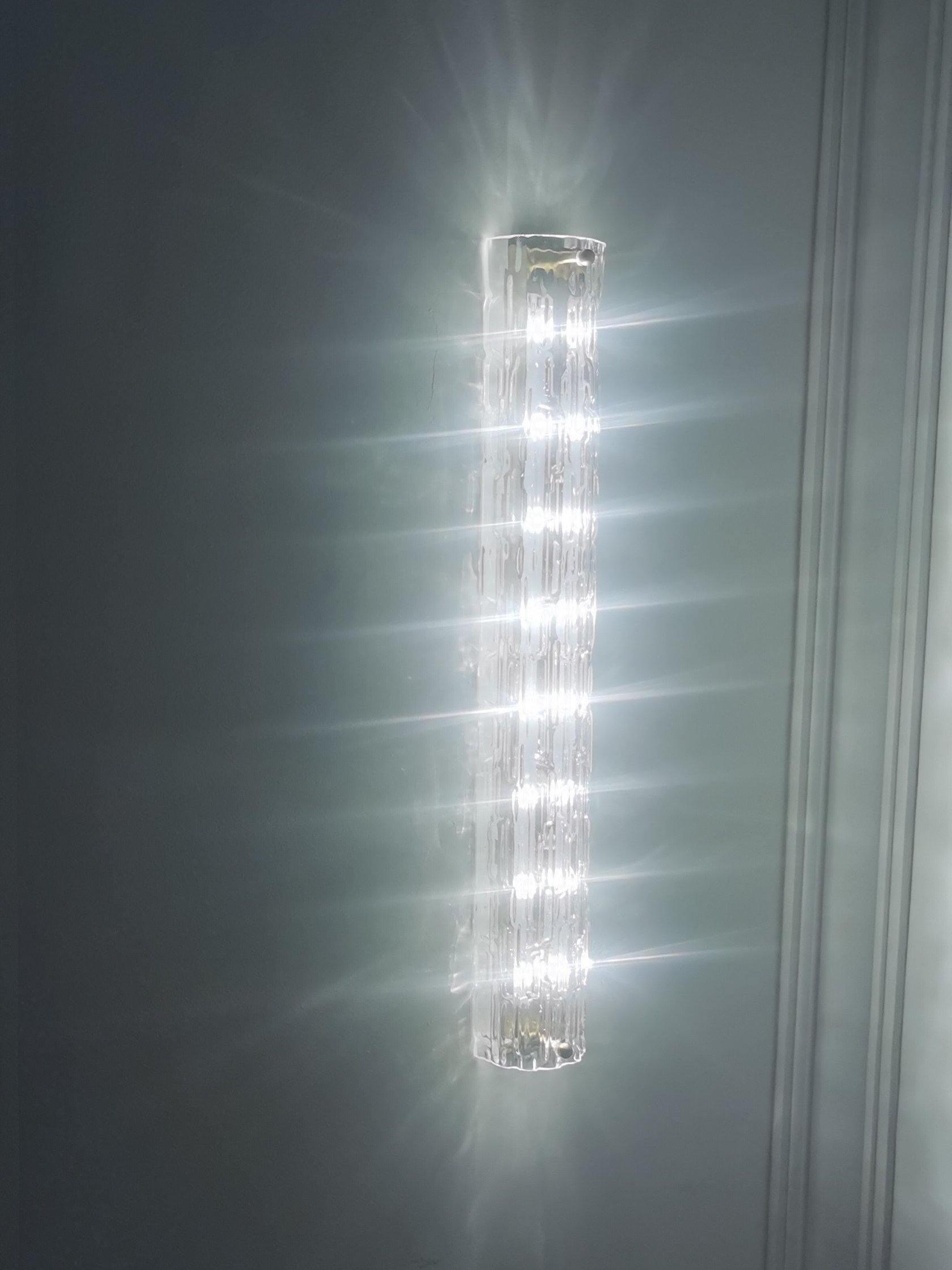 Bright glass wall light casting rays on dark grey wall