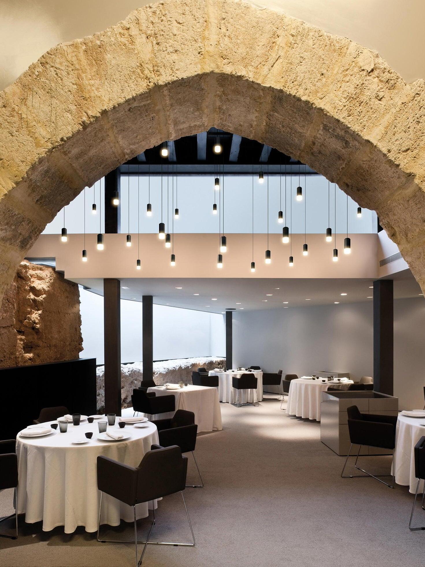 Hanging black pendant heads beneath a stone arch above round restaurant tables