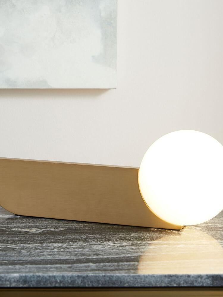 Lit globe lamp laid horizontally on a dark marble-looking surface beside its gold-colour blade