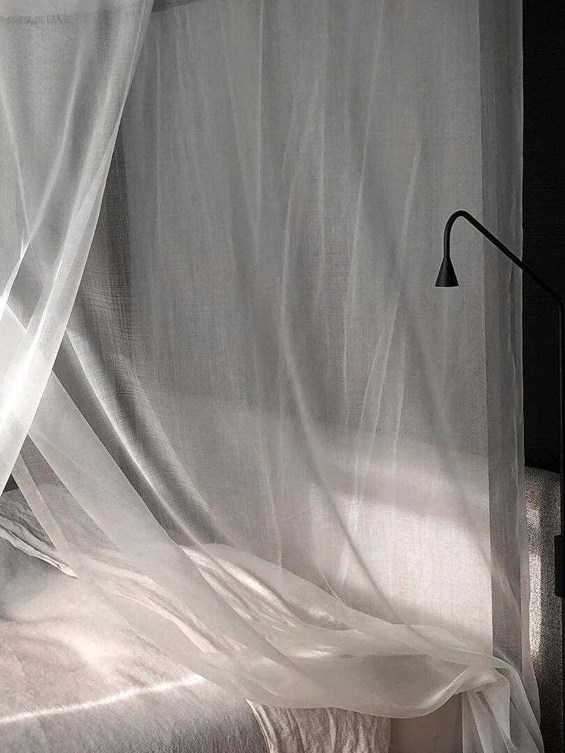 Black wall-light head near sheer bed curtains