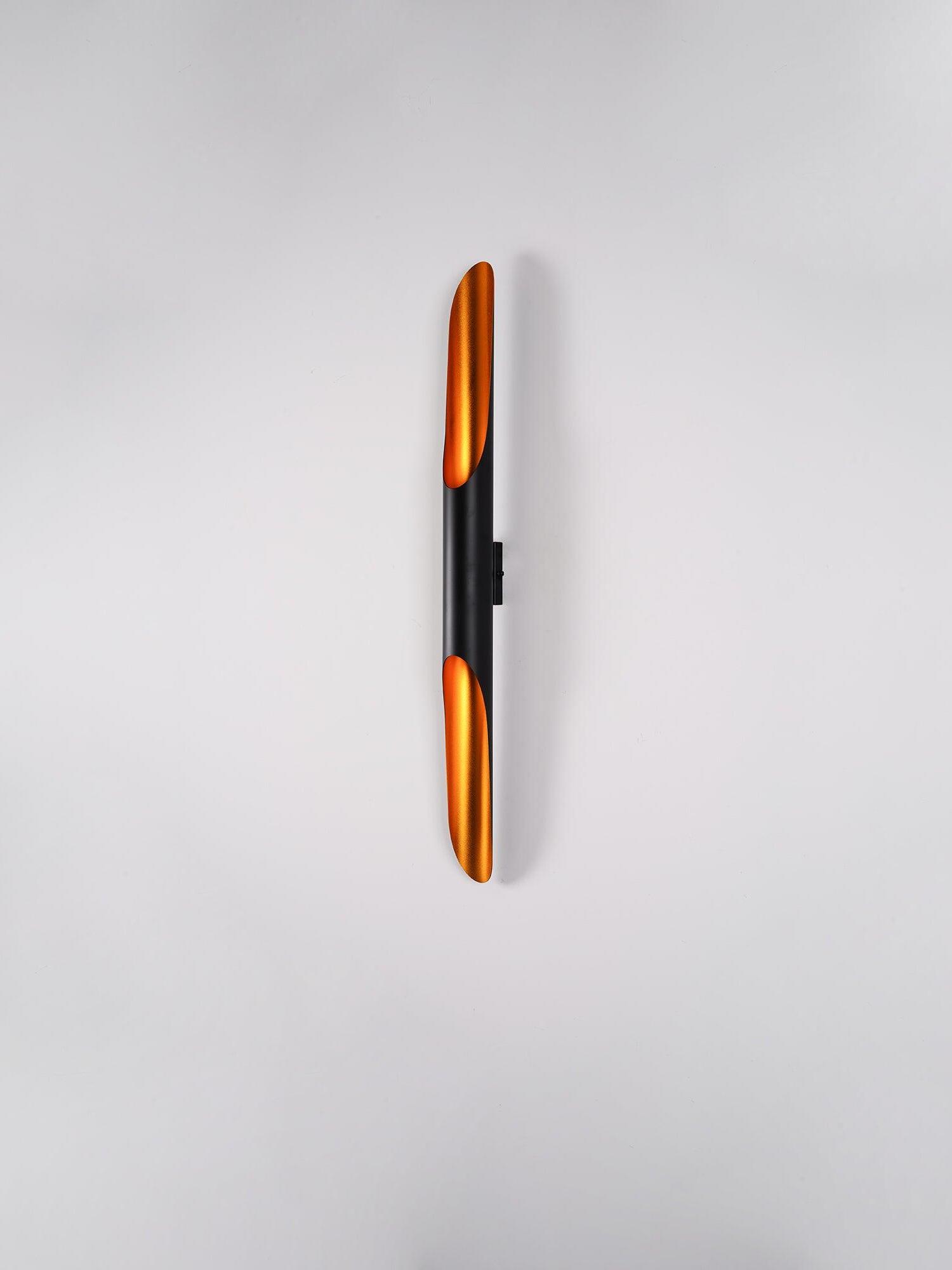 Oblique view of a black tubular wall light with glowing gold openings and visible wall plate