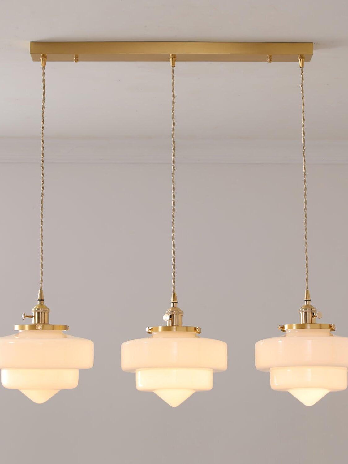 Front view of three illuminated Atlas Model A shades under a long brass canopy, with the outer heads partly cropped