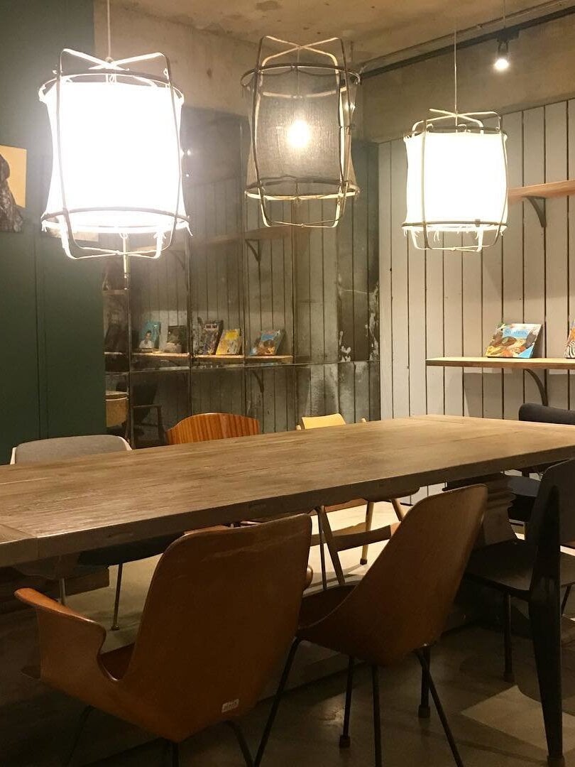 Three bamboo lantern pendants with white cloth and transparent dark covers above a long wooden showroom table