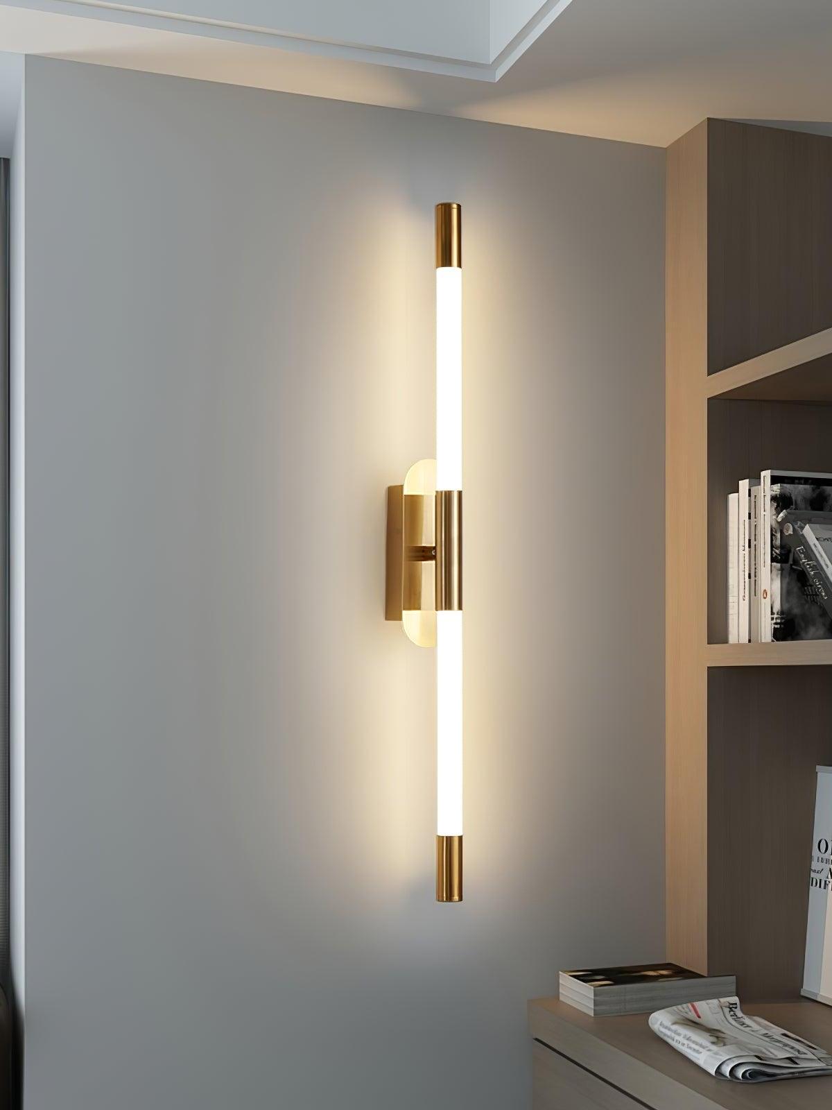 Vertical gold-finish Agnes wall light beside open shelving on a pale wall