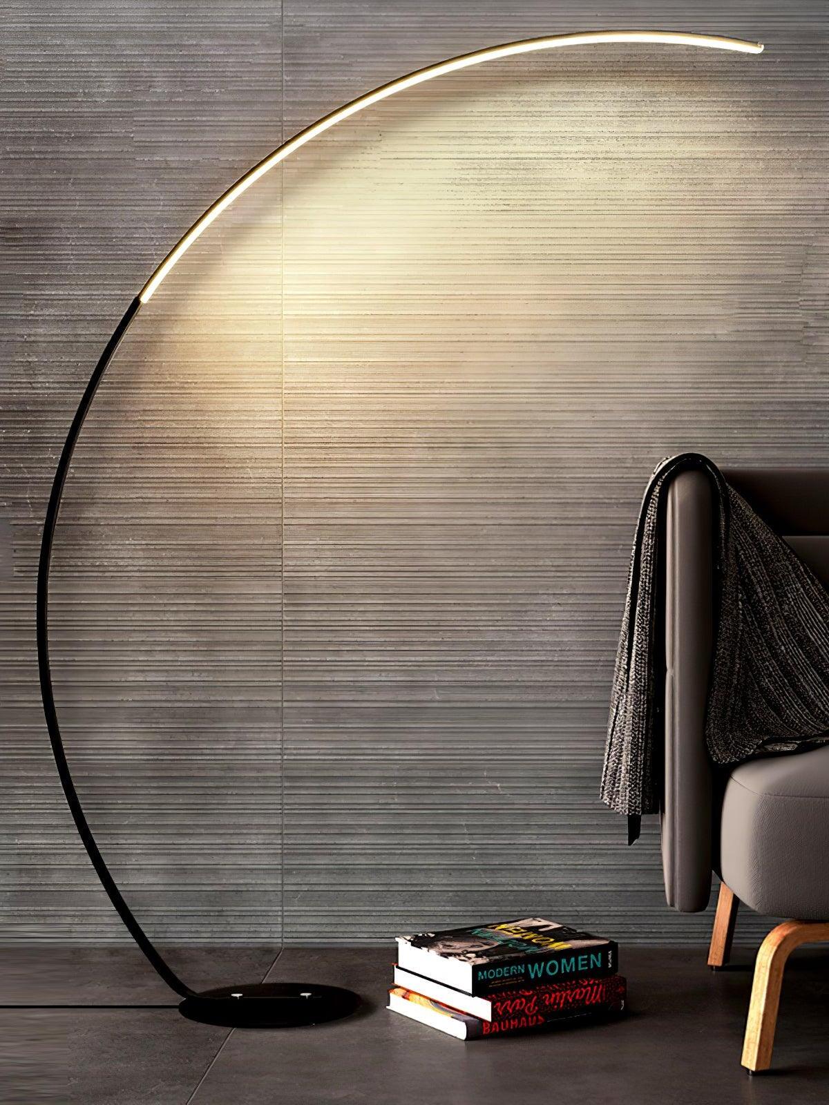 Black curved floor lamp beside chair and books