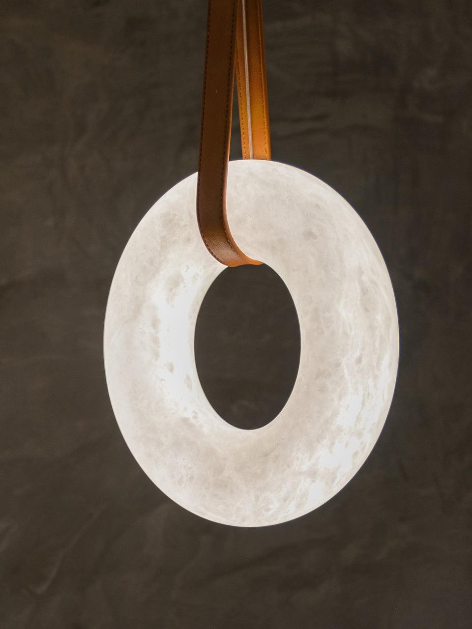Upright white alabaster ring held by a brown strap