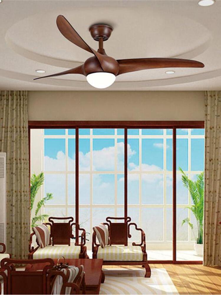 Brown three-blade ceiling fan with bright circular light above wood-framed seating beside large glass doors