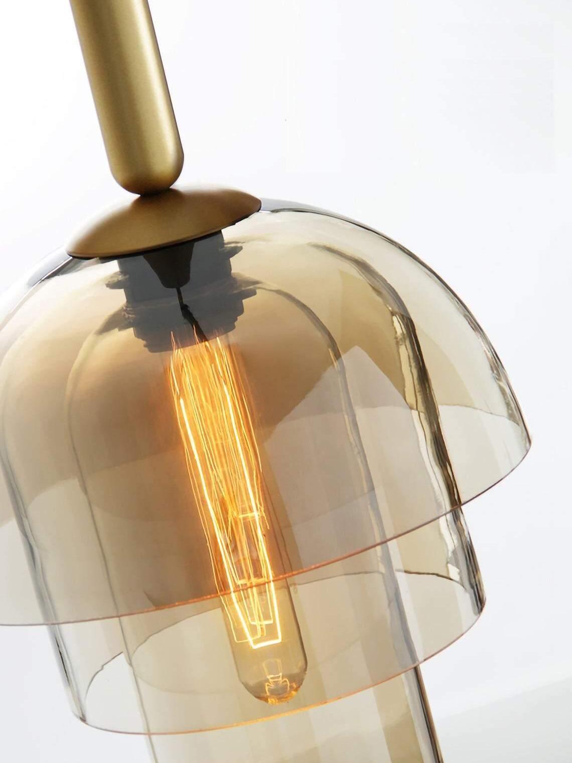 Angled detail of amber domed glass and a lower cylinder around a long glowing filament bulb beneath a gold-tone fitting