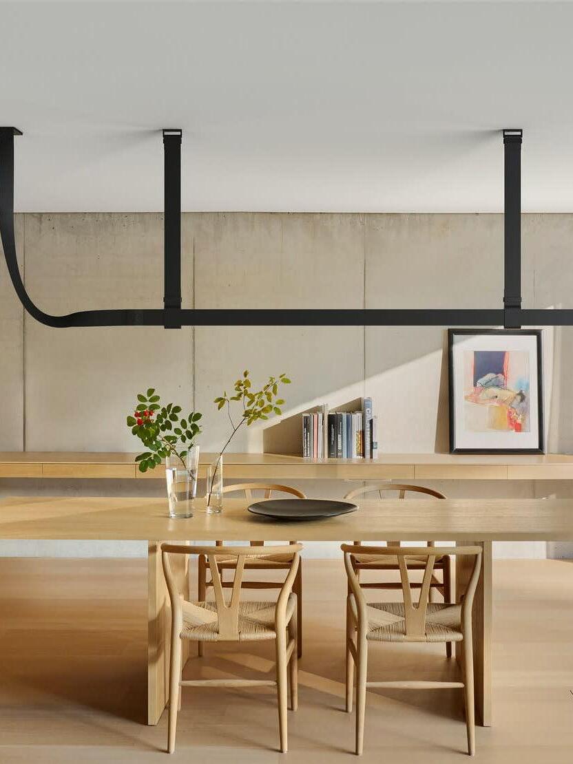Black horizontal pendant over a wood dining table with flowers and chairs, against a pale cabinet and framed artwork