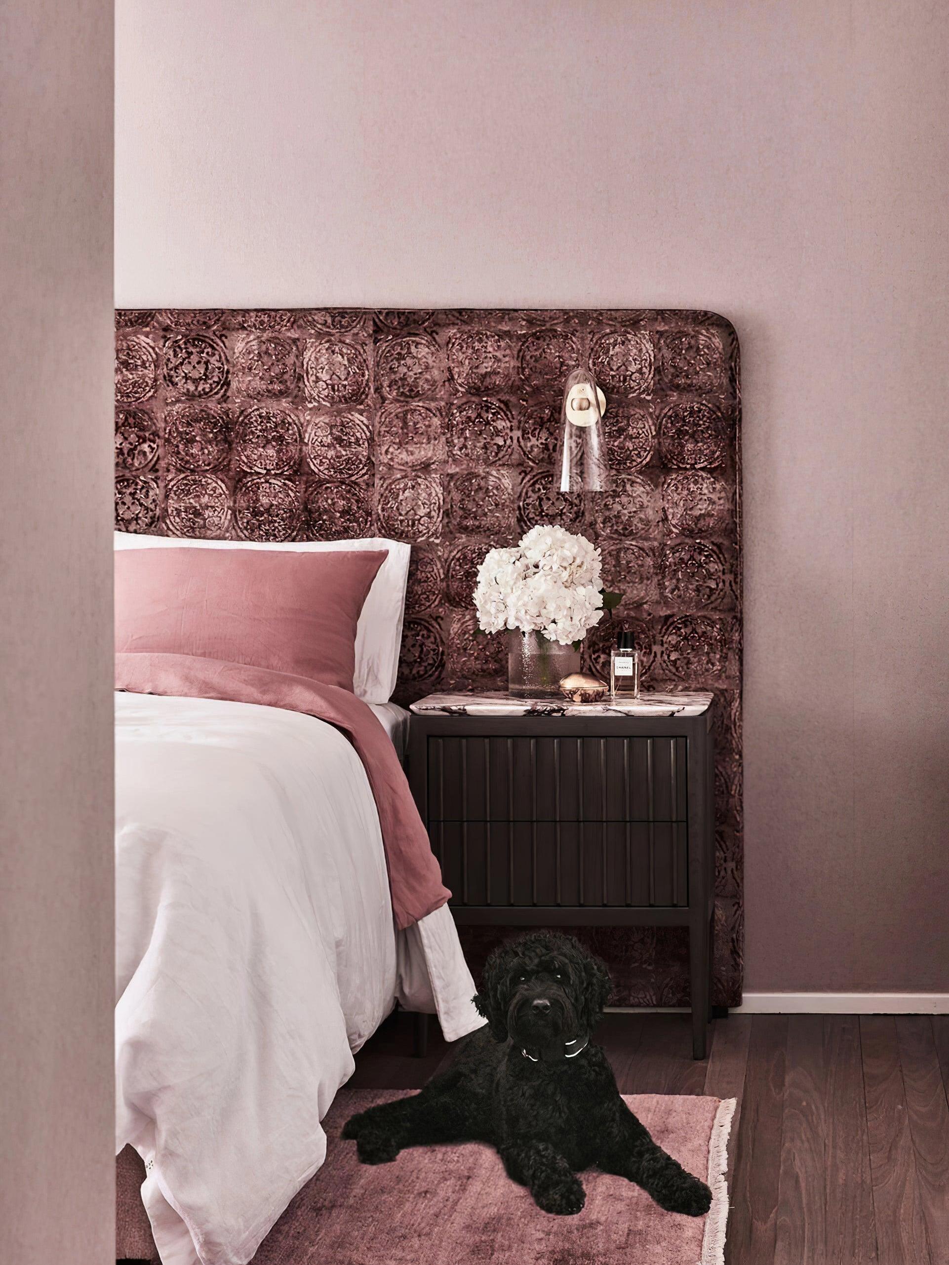 Clear conical wall light beside a pink upholstered bed