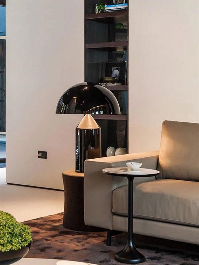 Glossy black dome lamp with a gold-tone cone area beside a taupe sofa and shelves
