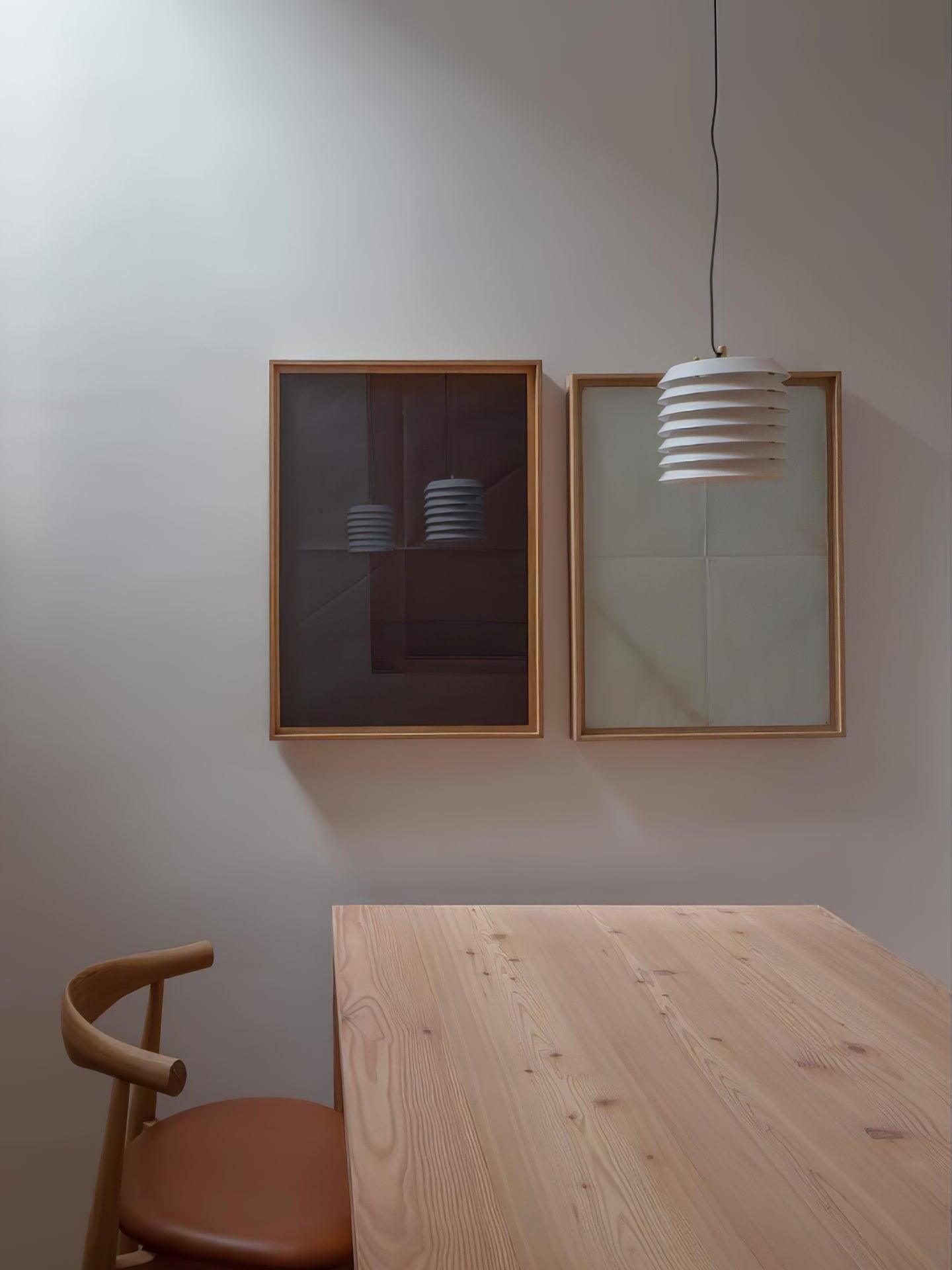 Unlit white layered pendant above wood table in front of framed art