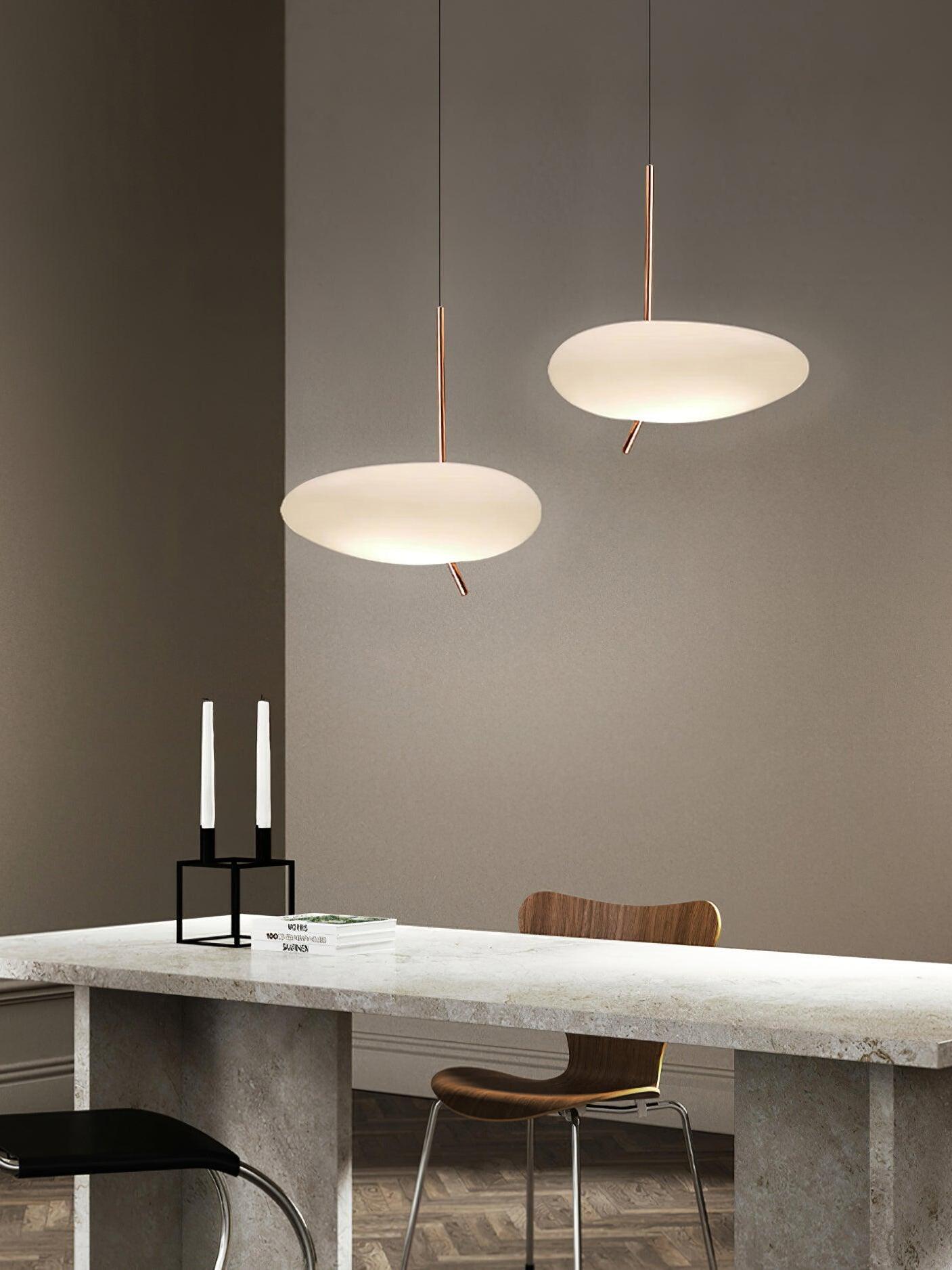 Two glowing white shades on slim suspension cables above a dining table and chairs