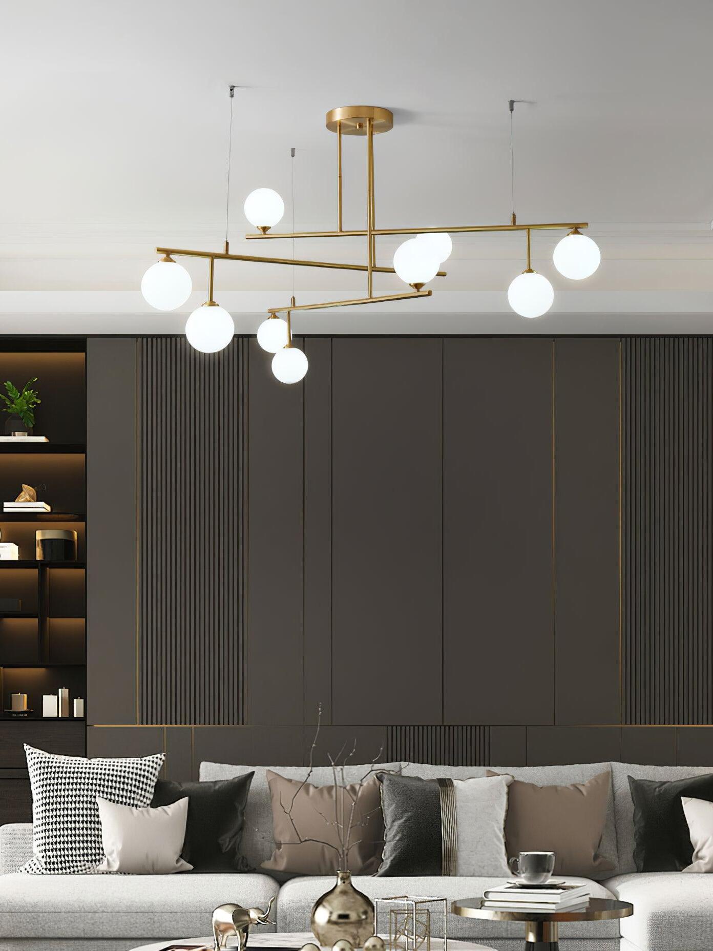 Illuminated Arteriors chandelier above a grey sofa, with tall dark cupboards behind the seating