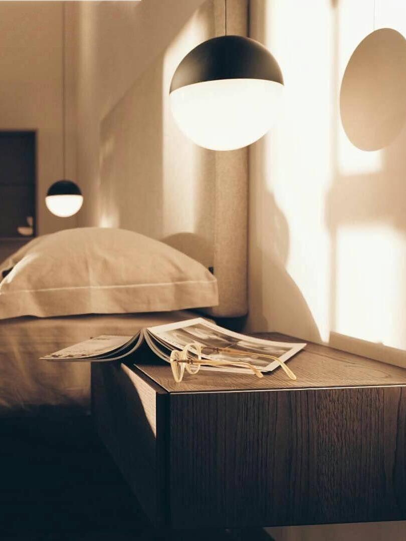 Black-topped glowing white globe beside a bed and wood cabinet with glasses and reading papers