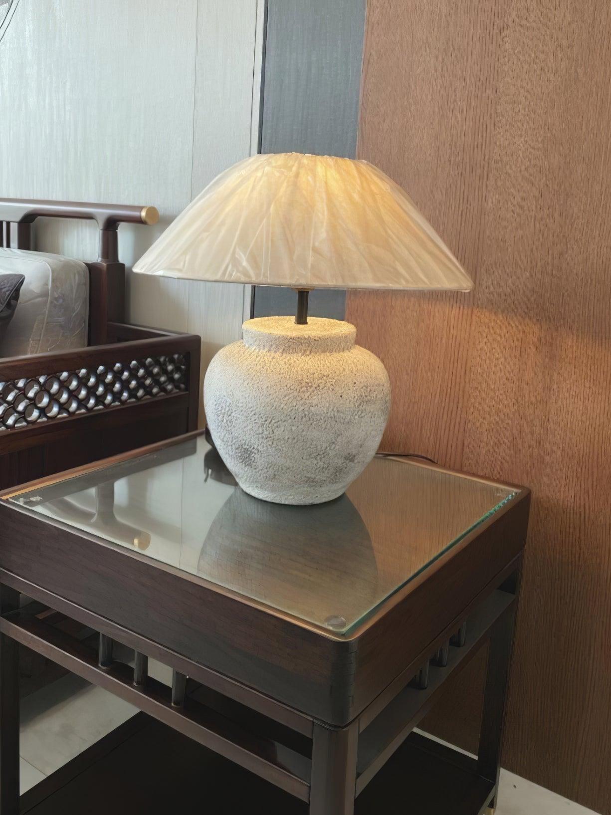 Pale urn table lamp on dark side table beside chair