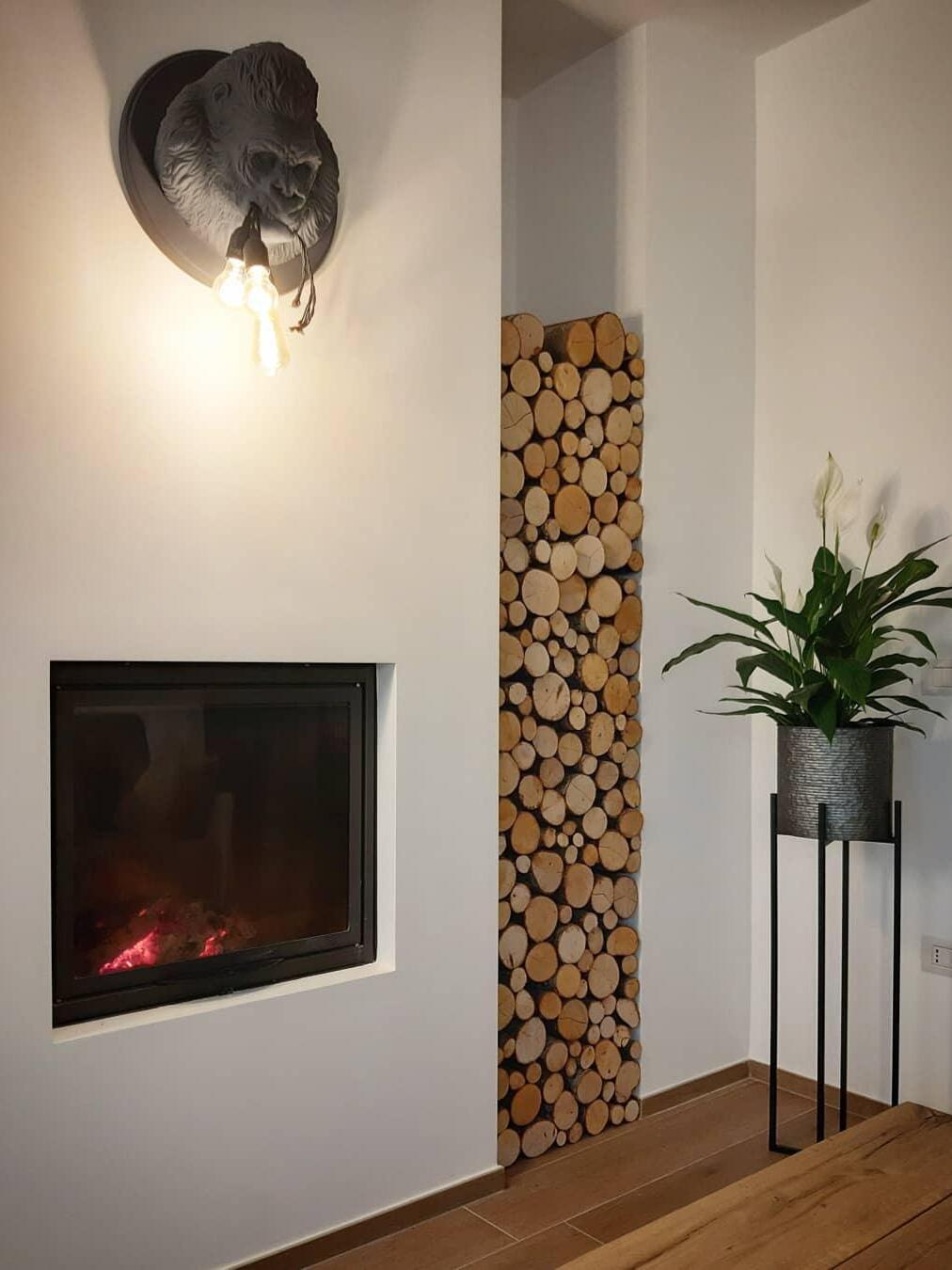 Dark gorilla light above fireplace in tall room with wood stack and plant