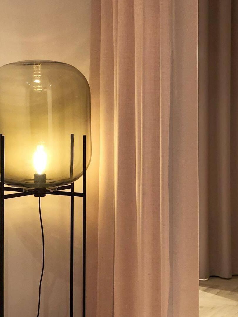 Close view of a lit bulb inside amber glass beside cream curtains.