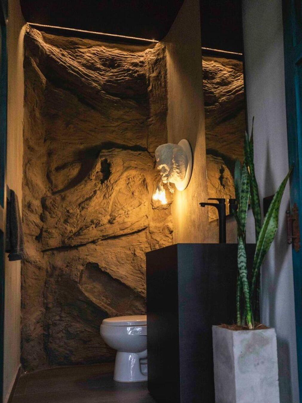 Tall washroom view with rock wall, illuminated white gorilla relief and plant